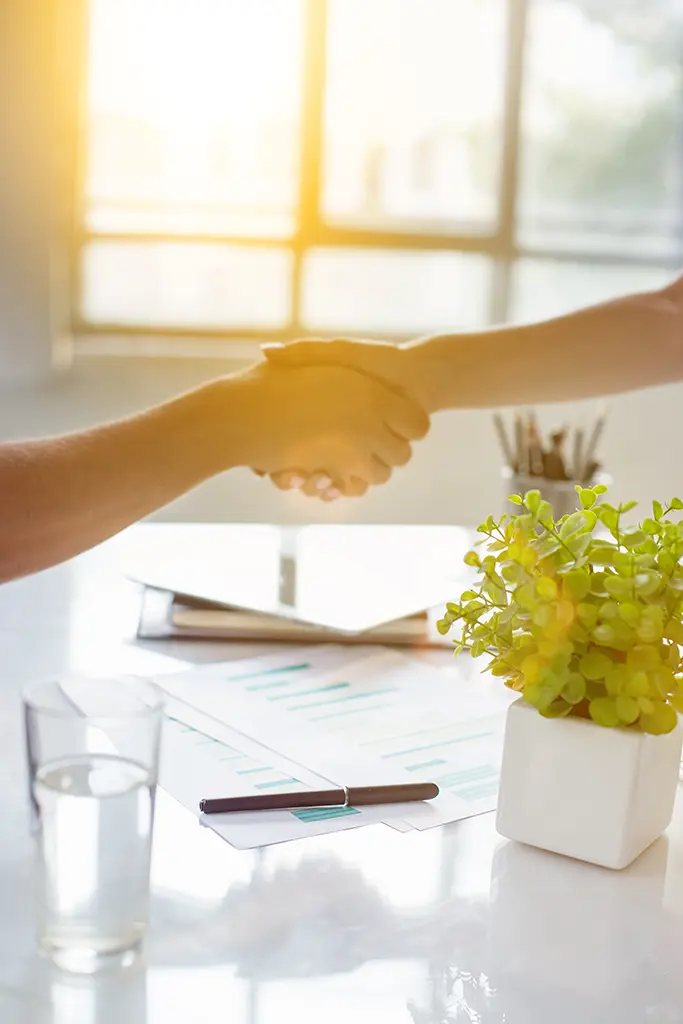 Two professionals shaking hands across a desk in a bright office, symbolizing successful business partnerships and agreements, Advanced Employment Services. Privacy policy ensures confidentiality in all interactions.