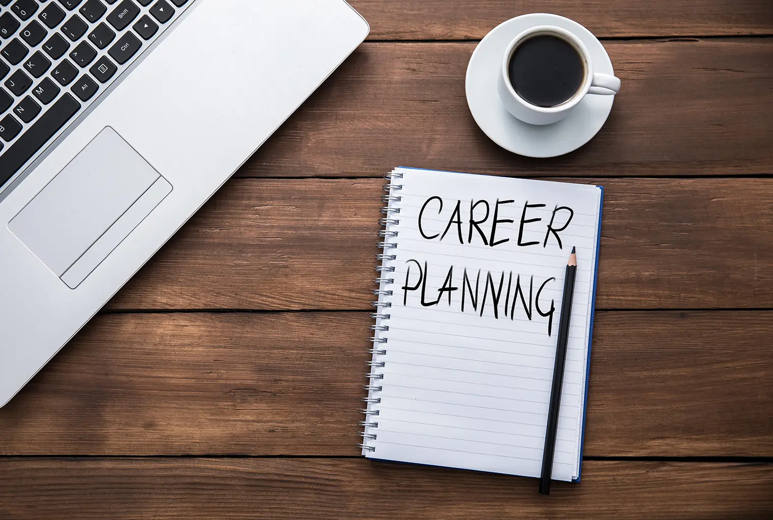 Career planning goals outlined in a notepad on a desk with a laptop and coffee, representing the importance of setting career goals with Advanced Employment Services.