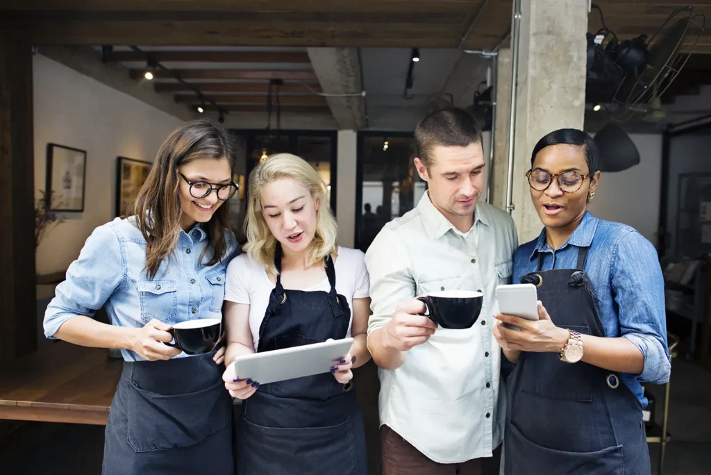 A group of colleagues in a coffee shop using digital devices to discuss delegation strategies, supported by Advanced Employment Services.