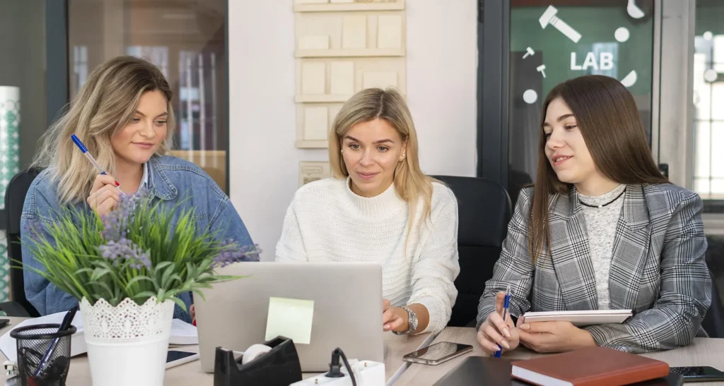 Three women collaborating on a project at a desk, representing teamwork and dedication at Advanced Employment. Learn more about their mission and services on the About page.