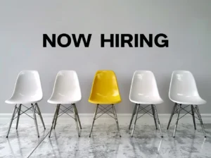 A row of white chairs with one yellow chair in the middle, under a 'Now Hiring' sign, illustrating the hiring process and the role of employers, with assistance from Advanced Employment Services.