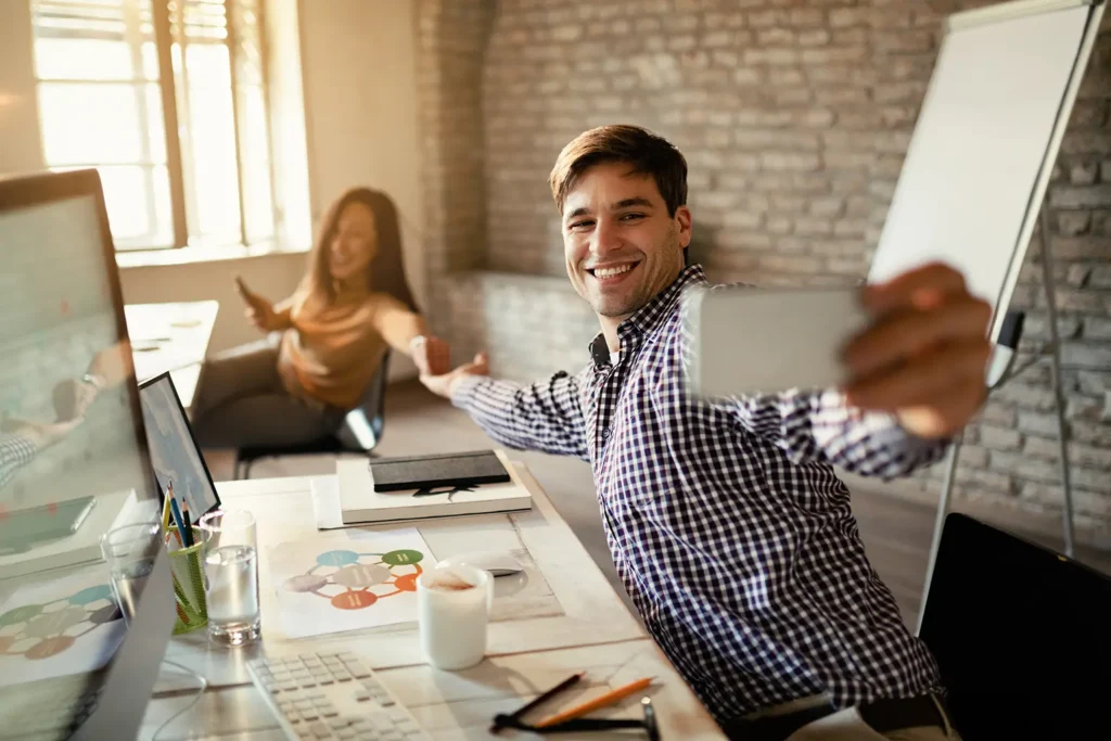 Young businessman and his colleague taking a selfie in a lively office environment, highlighting the importance of a motivating work culture and productivity with the support of Advanced Employment Services.